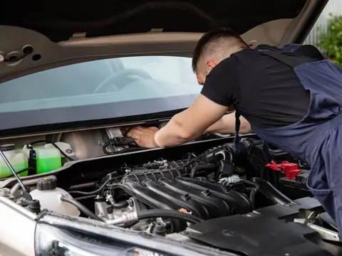 A technician working under the windshield of a silver SUV