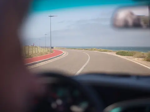 A coastal road seen through the windshield from the driver's seat